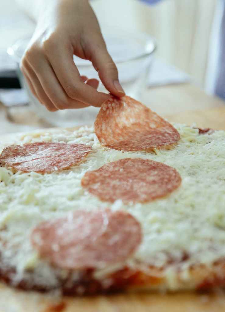 crop person with adding salami in pizza