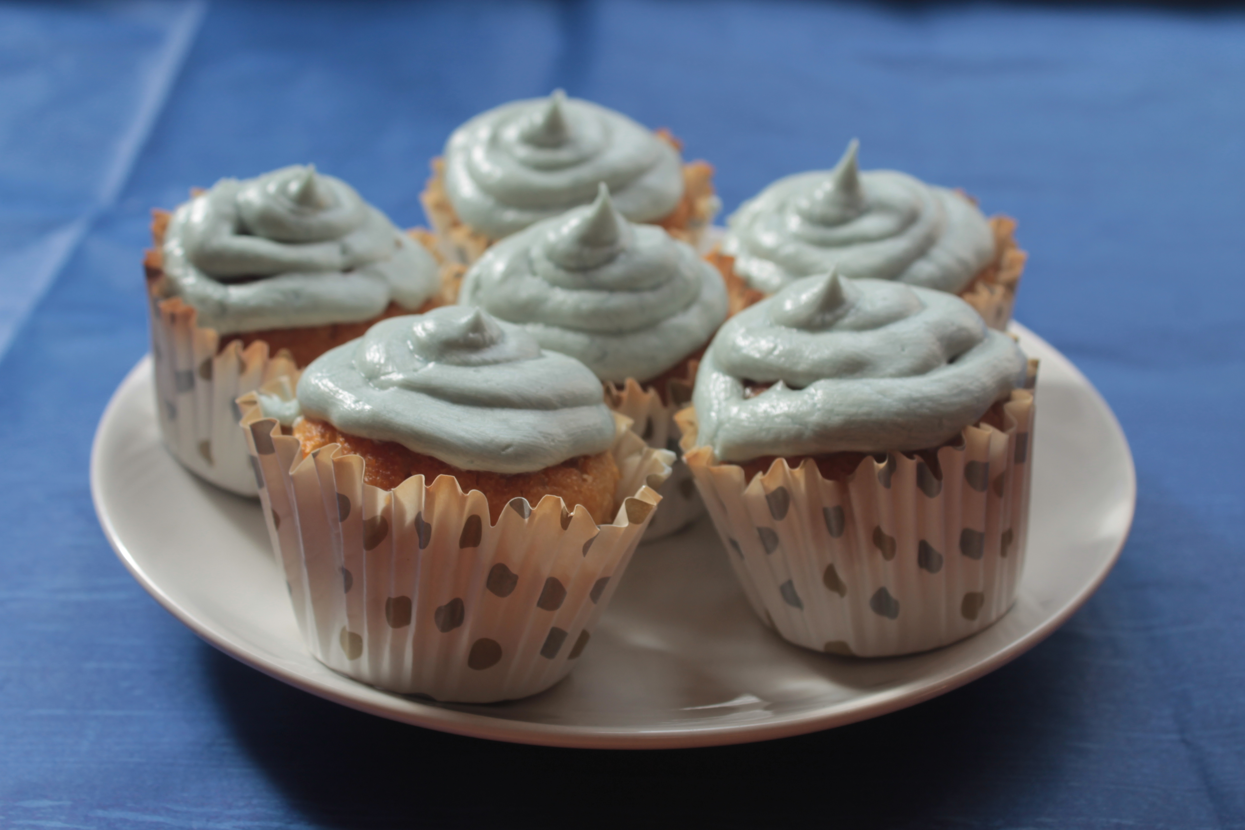 A white plate of cupcakes with pale blue icing