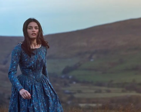 A picture of Emma Mackey, the actor who plays Emily Bronte in the 2022 movie 'Emily', pictured in a publicity shot from the movie, dressed in costume from the nineteenth century, walking across the moors above Haworth