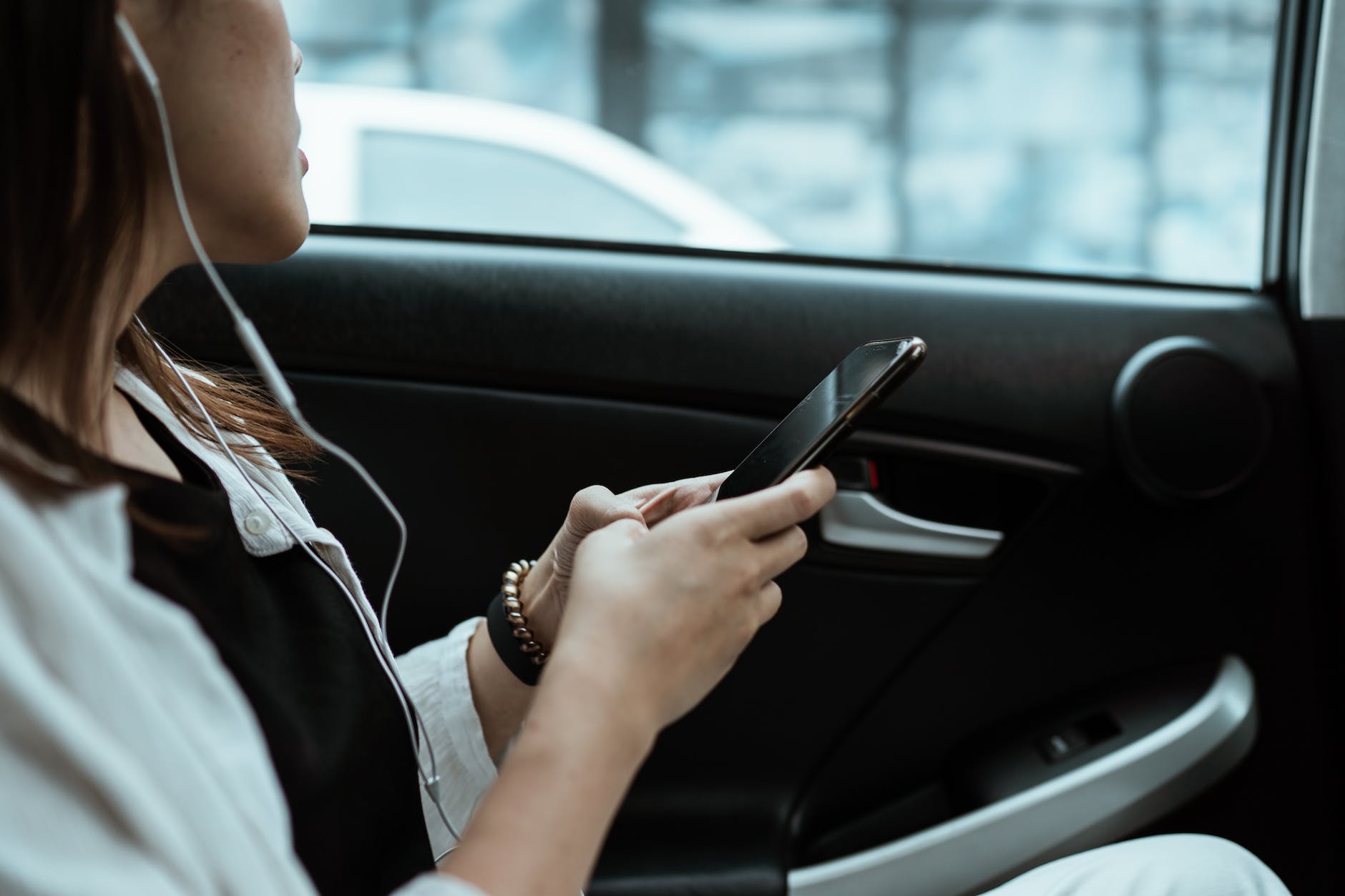 crop unrecognizable woman listening to music on smartphone in car